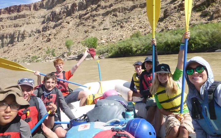 a group of students smile and raise paddles in the air while rafting on an outward bound trip